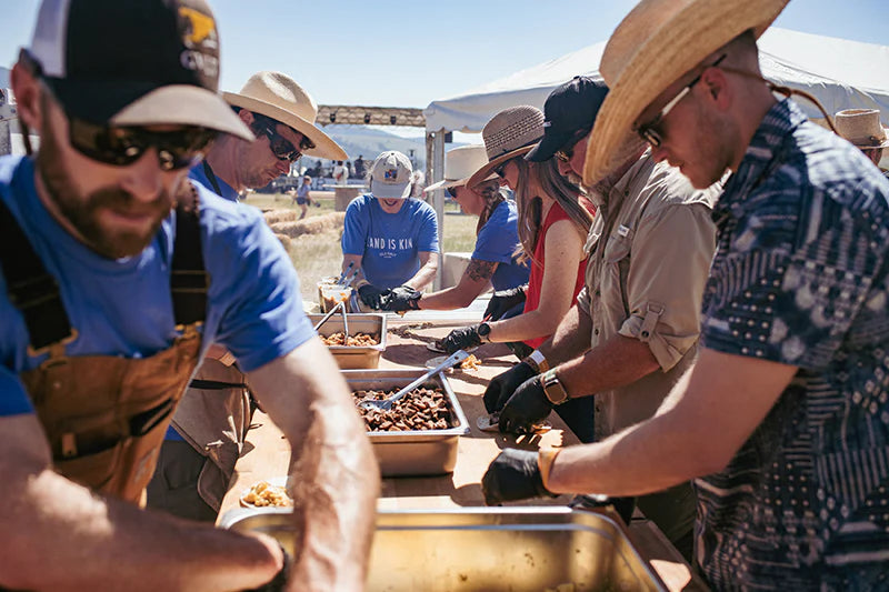 People in hats and gloves preparing food at outdoor tables under festival tents.